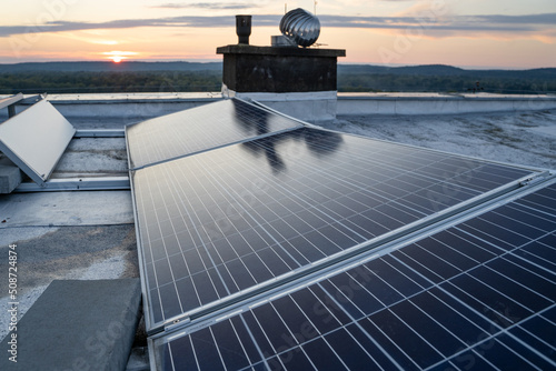 Solar panels located on the roof of the block. Green energy in modern city.  Sunset in the background