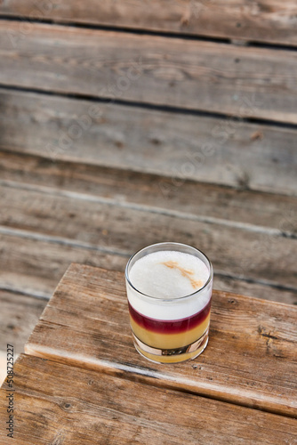 Yellow and purple sour cocktail served on a on a wooden bench patio