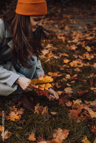 Young woman collecting colorful maple leaves from the ground into bunch