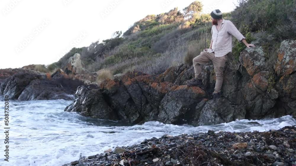 A fisherman waits on some coastal rocks for the high tide to scede so he can continue walking. A fisherman waits on some coastal rocks for the high tide to scede so he can continue walking.