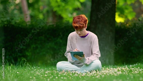 Non-binary gender person using a digital tablet in a park photo