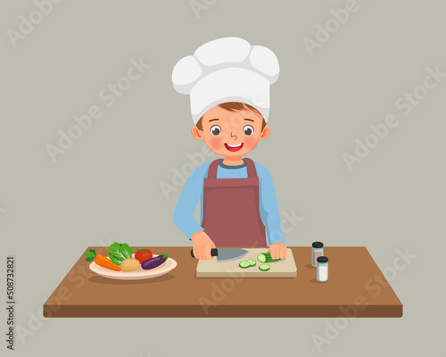 cute little boy chef cooking meal cutting slicing cucumber vegetable with knife in the kitchen