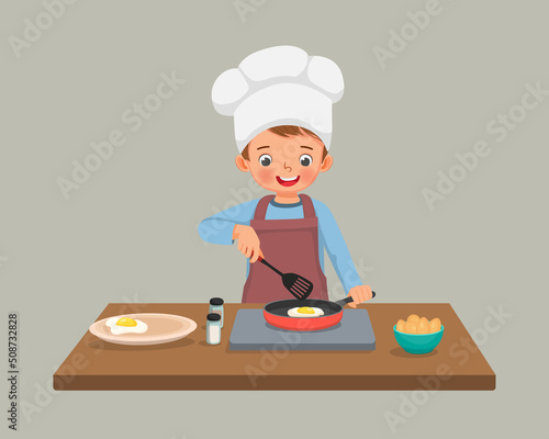 cute little boy chef cooking delicious fried egg with frying pan in the kitchen