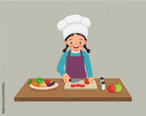 cute little girl chef cooking meal cutting slicing tomato vegetable with knife in the kitchen