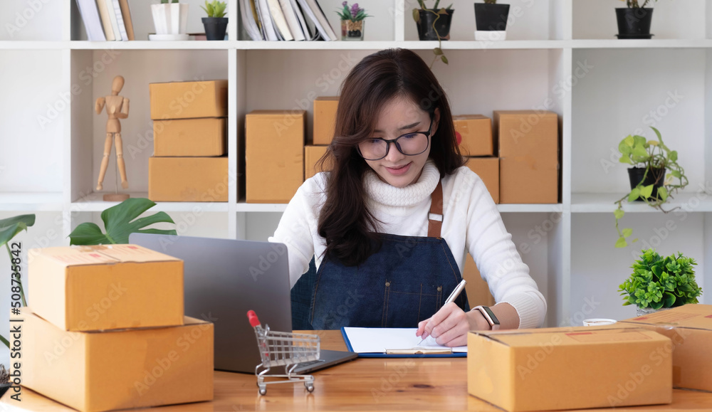 Young beautiful happy asian business woman owner of SME online using laptop receive order from customer with parcel box packaging at her startup home office, online business seller and delivery Young beautiful happy asian business woman owner of SME online using laptop receive order from customer with parcel box packaging at her startup home office, online business seller and delivery