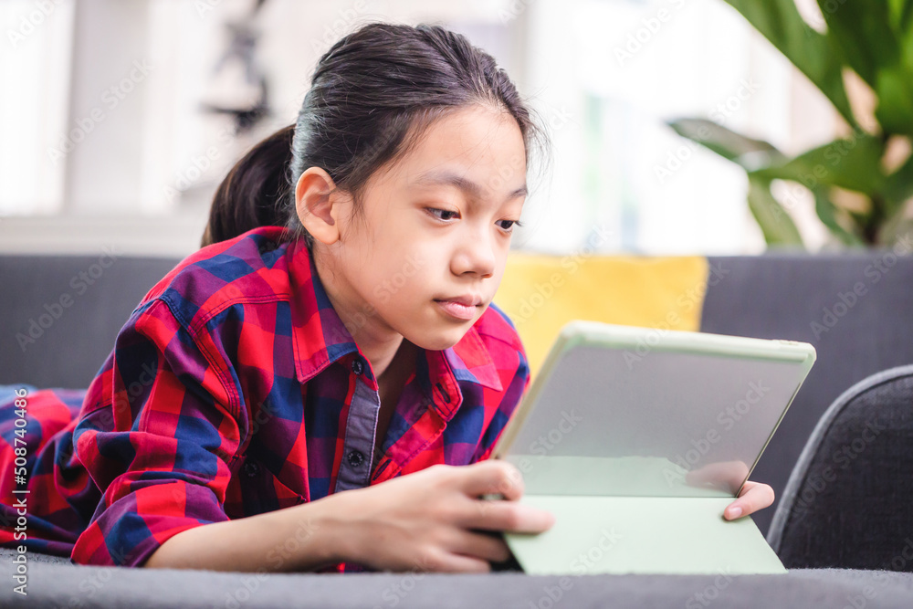 Happy child with digital tablet while resting on sofa, Asian kid girl in living room Happy child with digital tablet while resting on sofa, Asian kid girl in living room