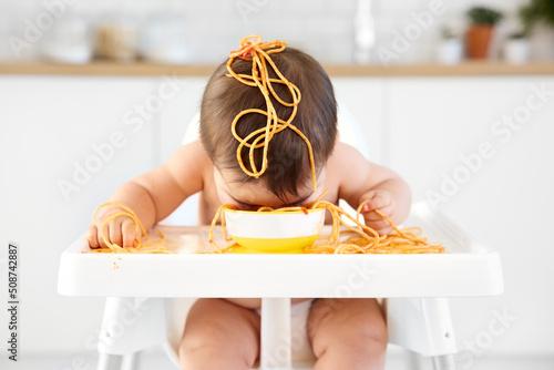 Funny baby eating spaghetti with face in bowl