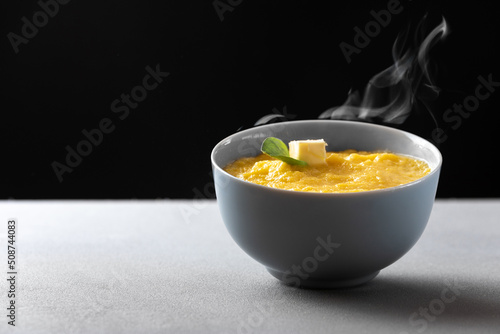 A traditional Italian dish is polenta. Plate gray with corn porridge polenta with a piece of oil on a gray background comes the steam from the cooked dish.