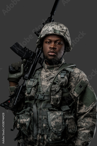 Photo of handsome military man of african ethnic armed with rifle isolated on gray.