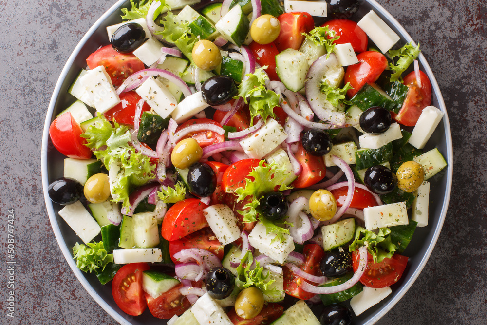 Healthy greek salad of fresh vegetables with tomatoes, lettuce, cucumbers, olives, feta cheese in plate on gray stone background. Healthy food, vegetarian dieting, close up top view from above