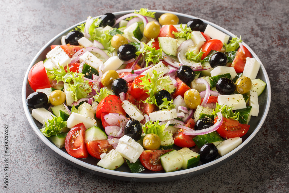 Healthy greek salad of fresh vegetables with tomatoes, lettuce, cucumbers, olives, feta cheese in plate on gray stone background. Healthy food, vegetarian dieting, close up