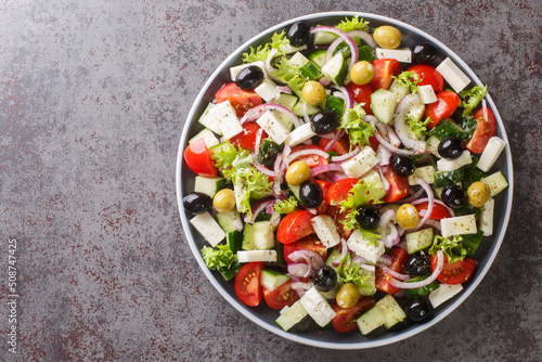 Classic Greek salad from tomatoes, cucumbers, onion with olives, oregano and feta cheese close-up in a plate on the table. Horizontal top view from above