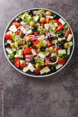 Healthy food Greek salad of fresh cucumber, tomato, sweet pepper, lettuce, red onion, feta cheese and olives with olive oil. Vertical top view from above