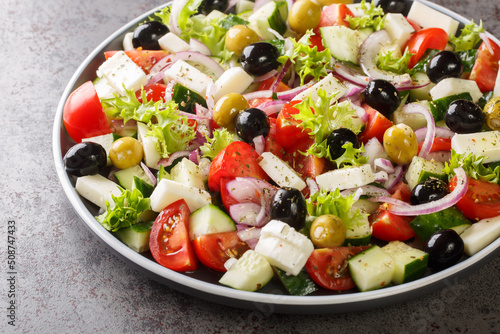 Classic Greek salad from tomatoes, cucumbers, onion with olives, oregano and feta cheese close-up in a plate on the table. Horizontal