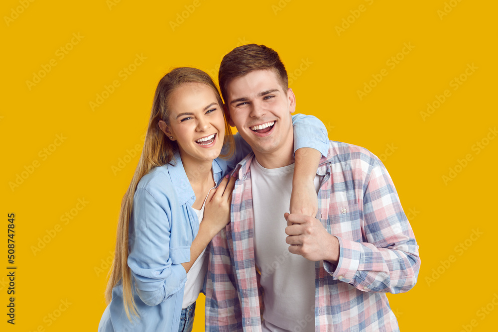 Naklejka premium Portrait of happy excited smiling young caucasian couple isolated on orange background. Joyful girlfriend and boyfriend in casual clothes hugging laughing at camera. Concept of love and youth.