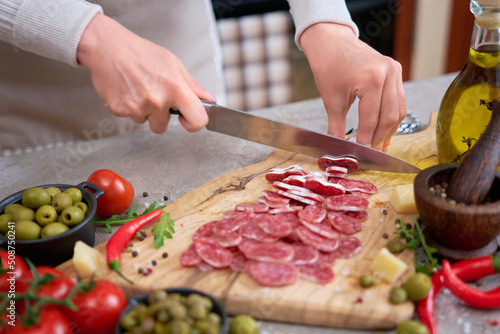 Woman slicing Spanish sausage fuet salami with knife on a domestic kitchen