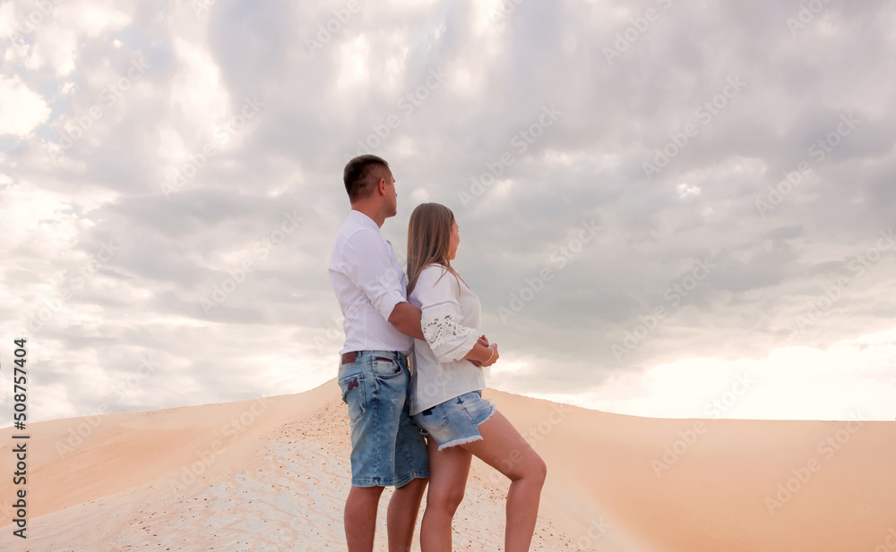 husband hugs his wife. romantic casual couple are standing close in profile with hug and looking apart in sand career background in desert at sunset. family relationship. lifestyle concept, free space