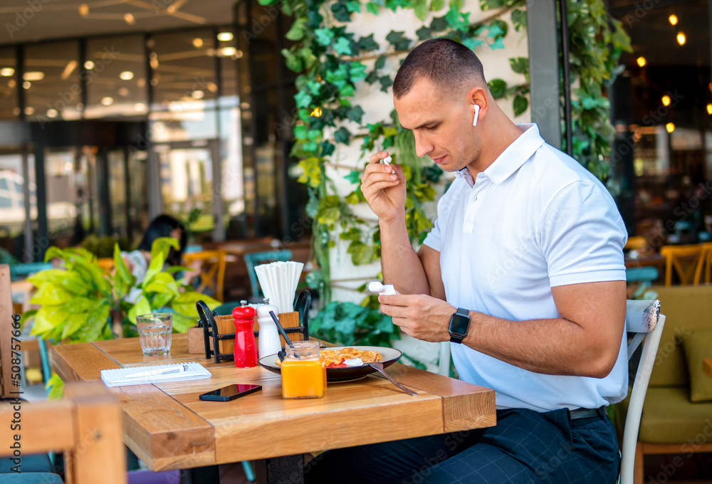 Young handsome businessman eating in a restaurant while using airpods Young handsome businessman eating in a restaurant while using airpods