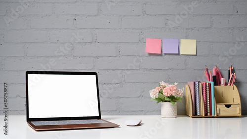 Stylish workplace with computer laptop, flower pot, stationery and sticky notes on brick wall. Blank screen for your advertise text © Prathankarnpap