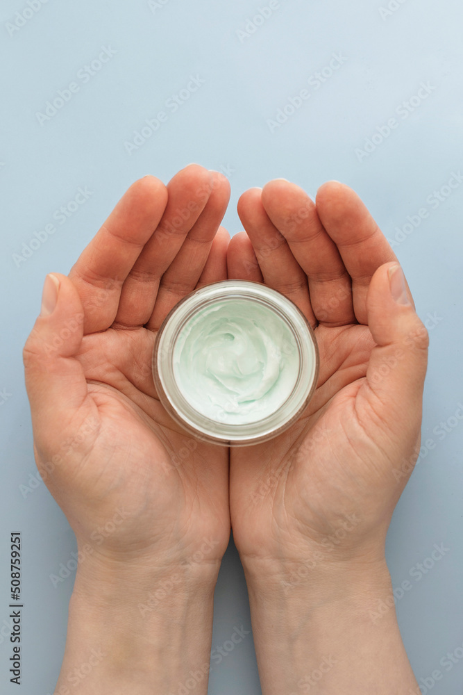 Skin care product. Female hand holding a face cream jar on pastel blue purple background. Beauty skin care product top view Skin care product. Female hand holding a face cream jar on pastel blue purple background. Beauty skin care product top view