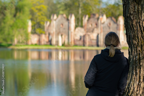 Girl near a trunk tree looking at Preili Manor Complex with one of the most fabulous city parks in Preili, Latgale, Latvia surrounded by lake or pond, green landscape photo