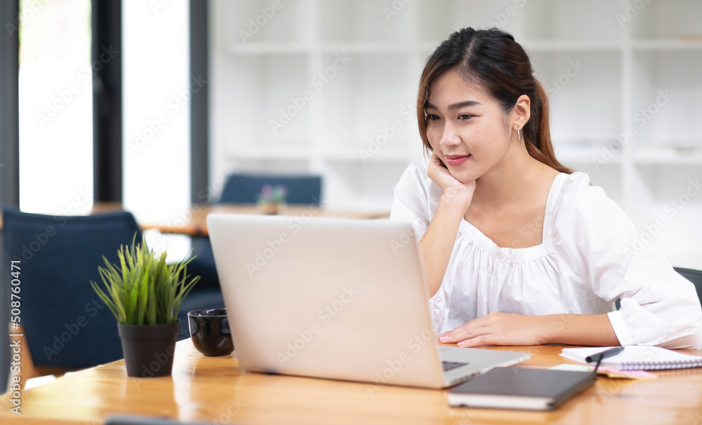 Happy young asian businesswoman sitting on her workplace in the office. Young woman working at laptop in the office. Happy young asian businesswoman sitting on her workplace in the office. Young woman working at laptop in the office.