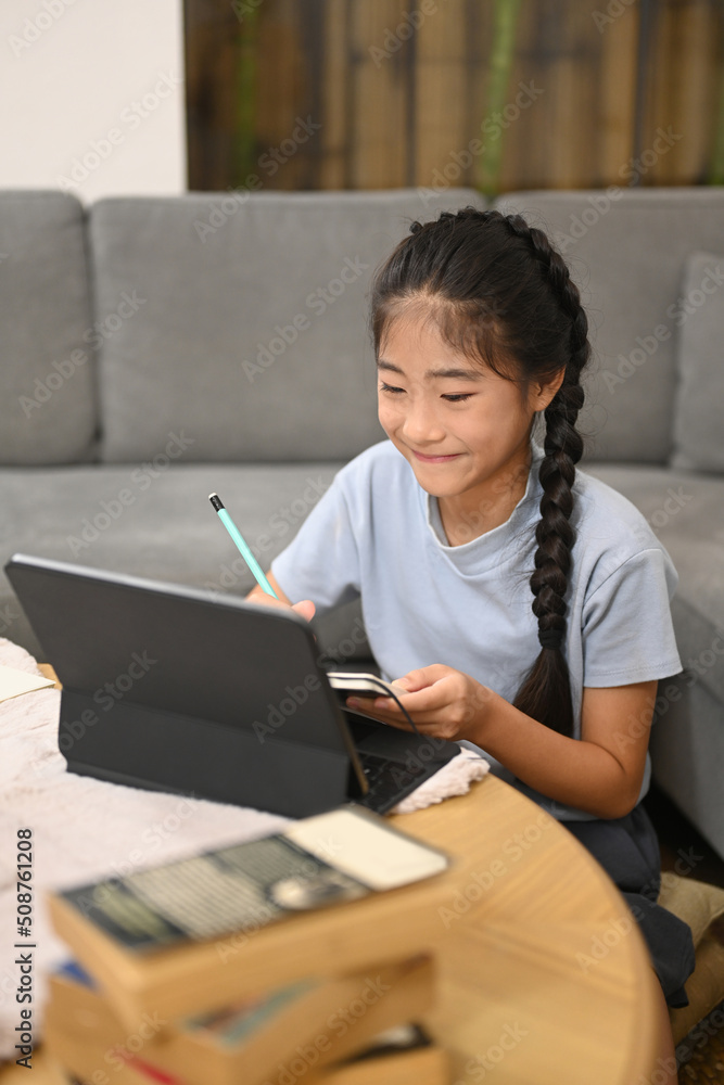 Happy girl watching learning online in virtual classroom on computer tablet, doing homework at home. E-learning, homeschooling concept Happy girl watching learning online in virtual classroom on computer tablet, doing homework at home. E-learning, homeschooling concept