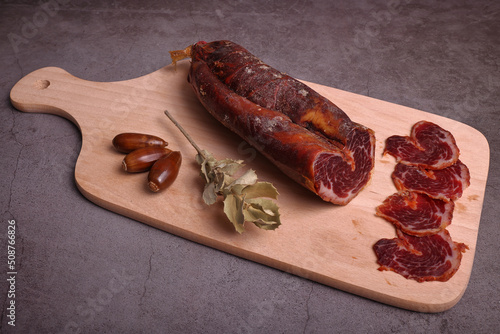 Iberian tenderloin on cutting board and dark gray table adorned with acorns and sprigs of oak photo