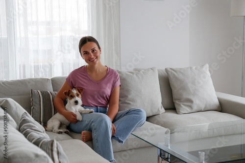 Portrait of young beautiful woman lying on the couch with her adorable wire haired Jack Russel terrier puppy. Loving girl with rough coated pup having fun. Background, close up, copy space.