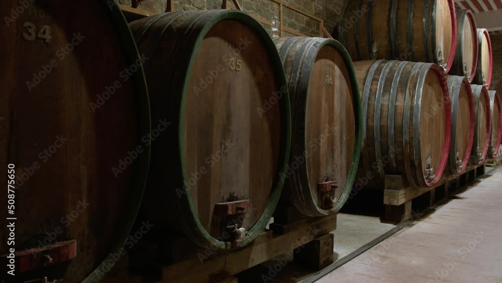 Wooden barrels for white and red wine aging, in rows and stacked, with golden and red written numbers, close-up dolly shot. Wooden barrels for white and red wine aging, in rows and stacked, with golden and red written numbers, close-up dolly shot.