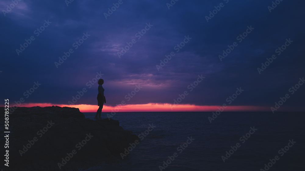 Silhouette of a woman watching sunset over distant horizon.