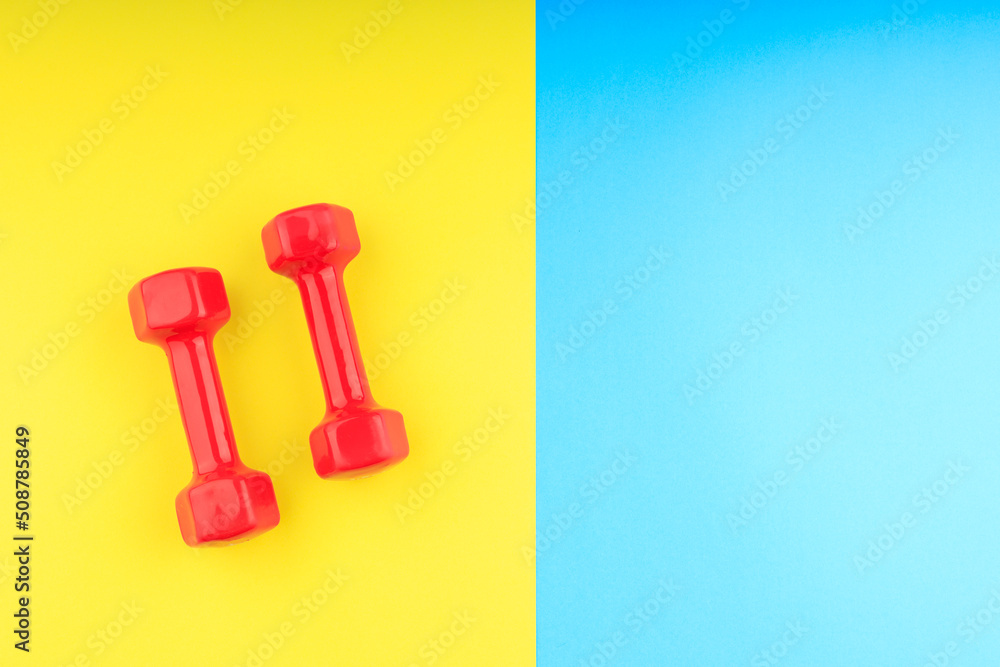 two bright red dumbbells for sports on a blue-yellow background two bright red dumbbells for sports on a blue-yellow background