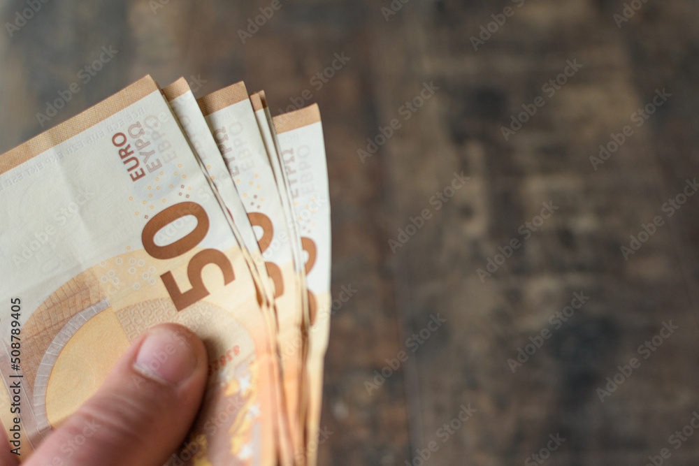 Cash payment. A man's hand holds out banknotes of 50 euros. Brown texture background. copy space