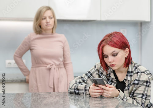 Unhappy mother looks at her teenage daughter, girl uses smartphone and ignores her mom. Family relationships
