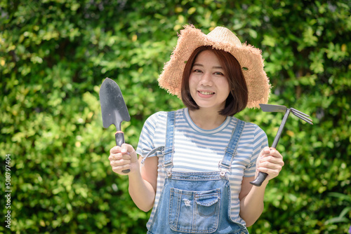 An Asian woman gardener is holding garden equipment tools.