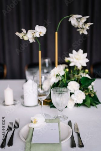 table setting for a wedding, white dishes on a wedding table with elements of green leaves and white flowers, themed decor. Menu card
