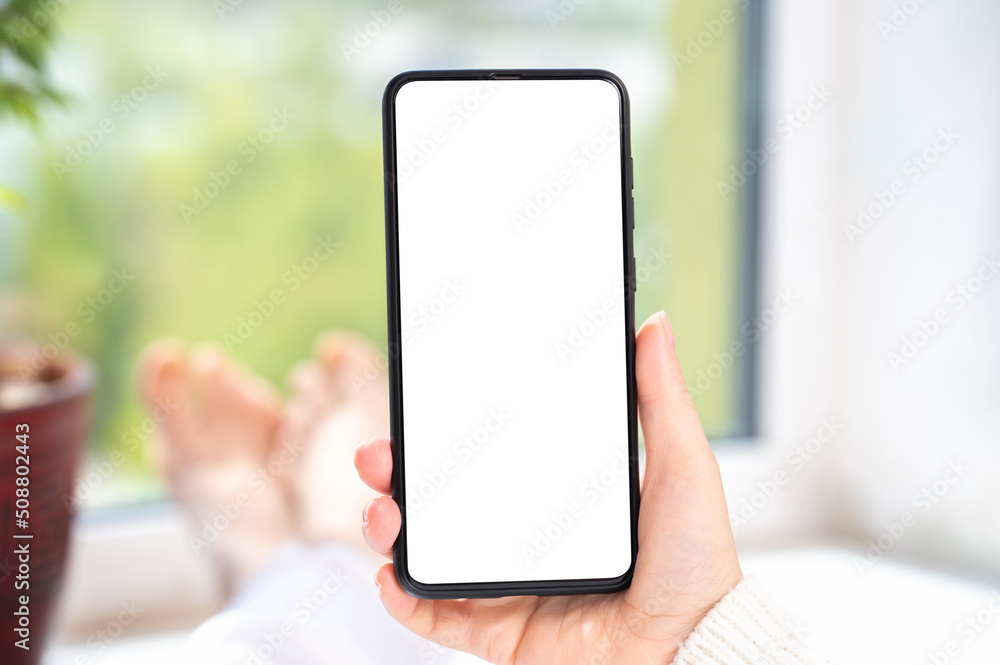 Use mobile shopping app, check social media news, texting mobile sms order food delivery sit near window at home in white clothes. Mockup cell phone. Use mobile shopping app, check social media news, texting mobile sms order food delivery sit near window at home in white clothes. Mockup cell phone.