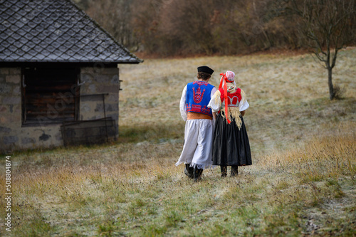 A couple dressed in traditional folk costume. Slovak costume in autumn nature. Old country cottage in the background. Young couple in folk costume walking in the garden