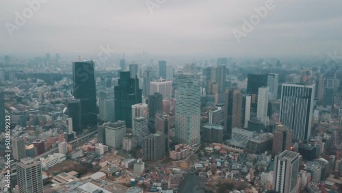 Aerial drone panning up away from the Tokyo city skyline in Japan on an overcast day with hazy smog filled skies and grey storm clouds above busy roads and skyscrapers photo