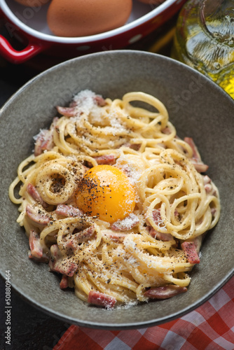 Close-up of italian spaghetti carbonara served with an egg yolk in a grey bowl, vertical shot, selective focus