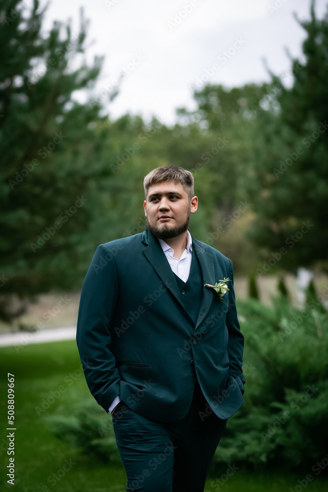 Stylish man in a green suit in front of a pool and a house in a green park. A garland of bulbs in a blur. Stylish man in a green suit in front of a pool and a house in a green park. A garland of bulbs in a blur.
