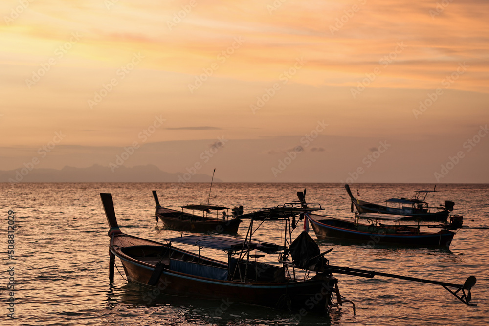 Stunning silhouette wooden fishing boats in Andaman sea during golden sunrise at Koh Lipe or Lipe island, Satun, Southern Thailand. Summer time or vacation travel concept.