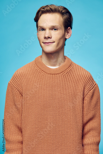 cute, handsome guy in an orange sweater stands on a blue background