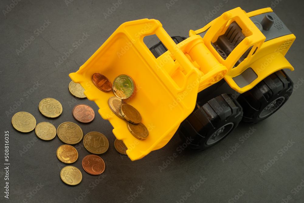 Yellow toy bulldozer, excavator carrying a lot of money - euro cent coins on dark background. Money digging, subsidies from European Union concept.