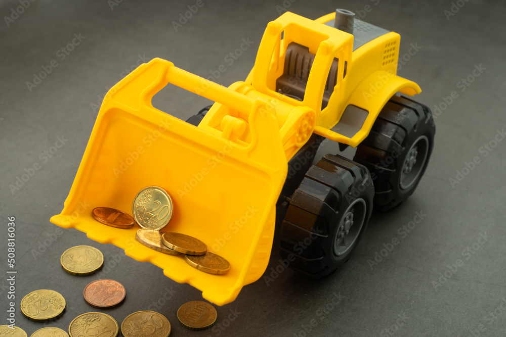 Yellow toy bulldozer, excavator carrying a lot of money - euro cent coins on dark background. Money digging, subsidies from European Union concept.