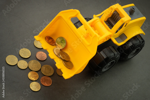 Obraz na płótnie Yellow toy bulldozer, excavator carrying a lot of money - euro cent coins on dark background. Money digging, subsidies from European Union concept. w salonie