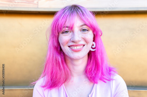 close up portrait of alternative woman withpink hair hanging out chilling and smiling standing isolated against  modern wood background wall. happy girl smiling at camera relaxing. lifestyle concept