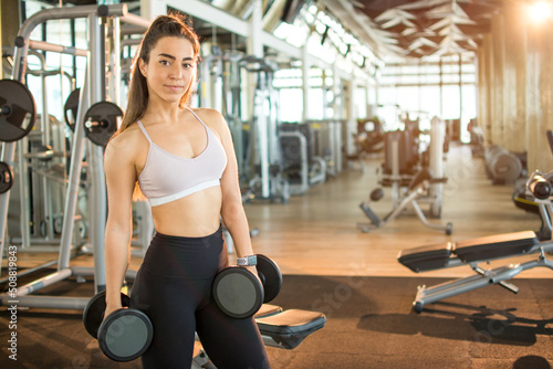 Portrait of attractive fitness woman with dumbbells posing in the gym