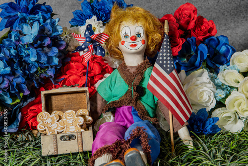 old clown doll holding American flag and pinwheel surrounded by flowers and gingerbread cookies