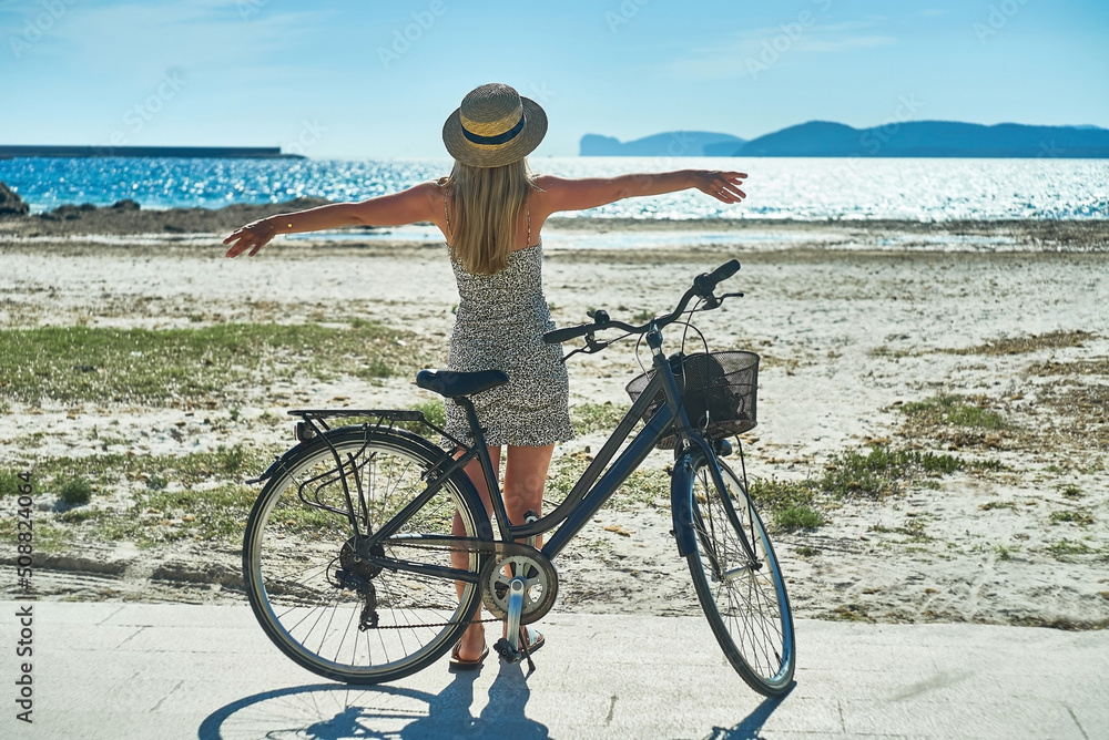 Fototapeta premium Carefree woman with bike riding on sand beach having fun, on the seaside promenade on a summer day.